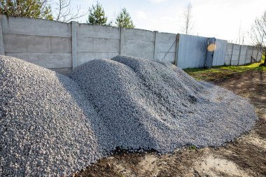 İnşaat için çakıl yığınları ve beton çitlerin yanında depolanan peyzaj.