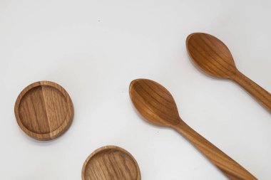 Ahşap mutfak kepçeleri ve yuvarlak kaseler beyaz arka planda simetrik olarak dizilmiş.