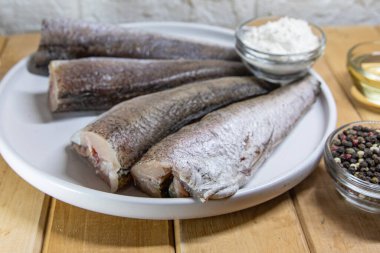 Çiğ balık filetosu beyaz tabakta ve ahşap masada baharatlar.