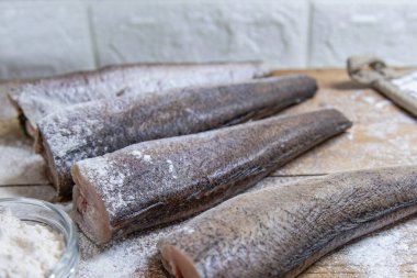 Tahta yüzeyde un ve baharatla kaplanmış çiğ balık parçaları.