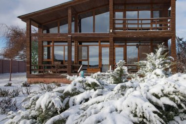 Karlı kış bahçesiyle çevrili geniş pencereli modern ahşap ev