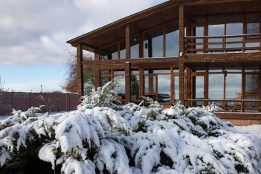 Karlı kış bahçesiyle çevrili geniş pencereli modern ahşap ev