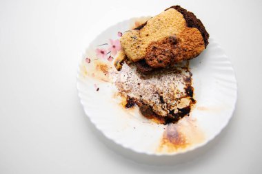 Beyaz tabakta pasta dilimi, kırıntılar ve çikolatalı tatlı.