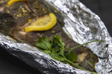 Limon dilimli tam pişmiş balık. Bitki ve baharatlar. Alüminyum folyoya sarılı.