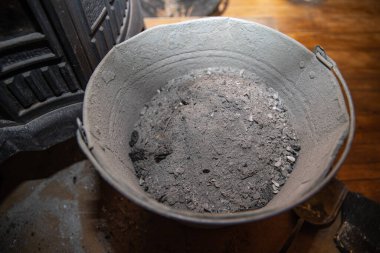 Ahşap zemin manzarasında odun sobası külleri olan metal kül kovası.