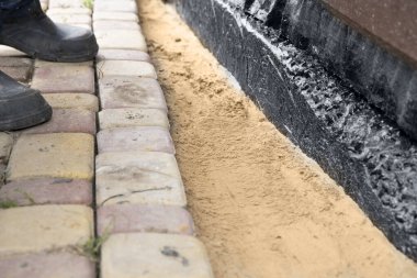 İnşaat temelleri boyunca kum tabanına beton kaldırım taşı döşeyen işçi elleri