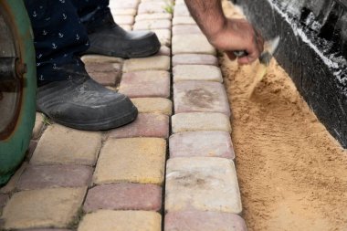 İnşaat temelleri boyunca kum tabanına beton kaldırım taşı döşeyen işçi elleri