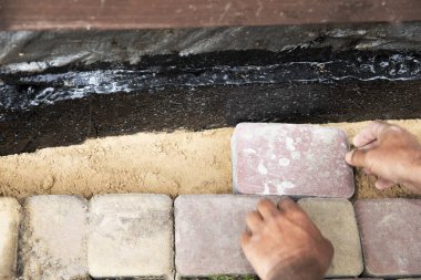 İnşaat temelleri boyunca kum tabanına beton kaldırım taşı döşeyen işçi elleri