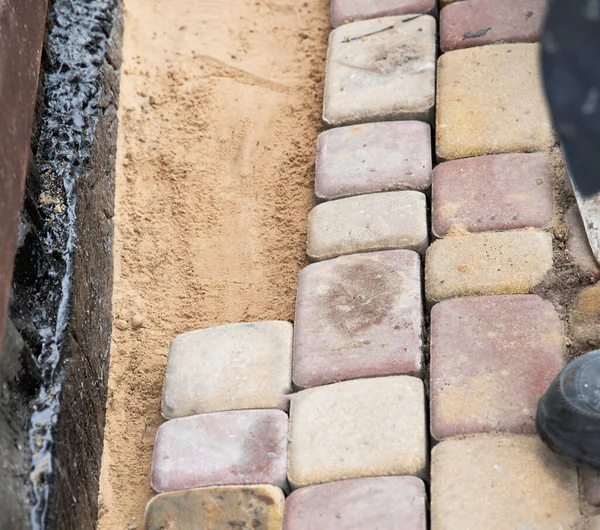 Beton kaldırım taşlarının kenarı. Yaya yolu boyunca kum tabanı var.