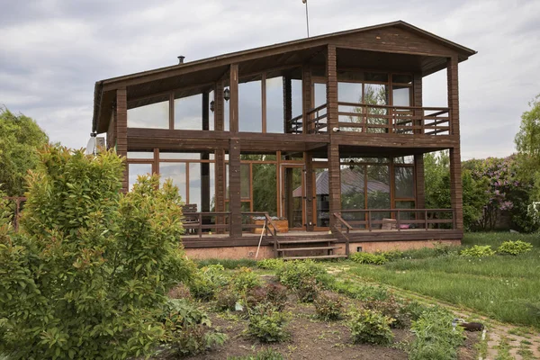 Bahçedeki büyük pencereli modern ahşap ev ağaç dallarının arasından görülüyor.