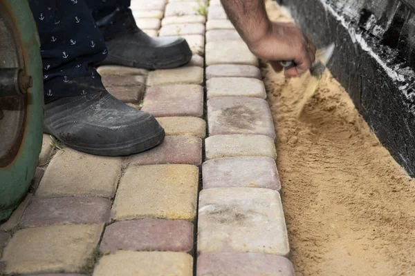 İnşaat temelleri boyunca kum tabanına beton kaldırım taşı döşeyen işçi elleri