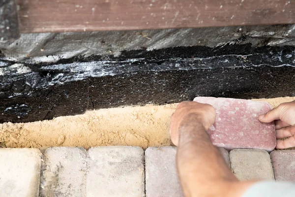 İnşaat temelleri boyunca kum tabanına beton kaldırım taşı döşeyen işçi elleri