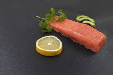 Avokado dilimli somon filetosu siyah taş tahtada limon ve otlar.