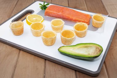 Avokado limonlu çiğ somon filetosu ve beyaz kesim tahtasında waffle fincanı.