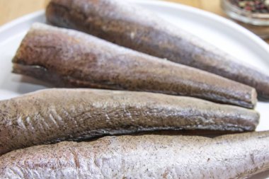 Mutfak masasındaki baharatlarla birlikte beyaz tabağa yerleştirilmiş çiğ balık porsiyonları.