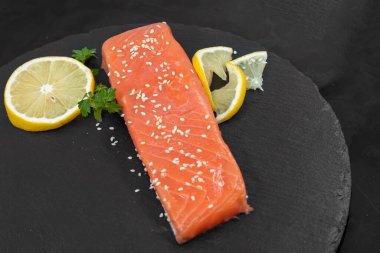 Koyu tahta kenarında limon dilimli çiğ somon filetosu.