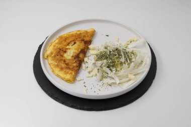 Kızarmış omlet, dilimlenmiş lahana peyniri ve beyaz tabakta kurutulmuş otlar.