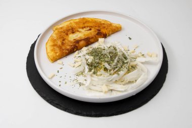 Kızarmış omlet, dilimlenmiş lahana peyniri ve beyaz tabakta kurutulmuş otlar.