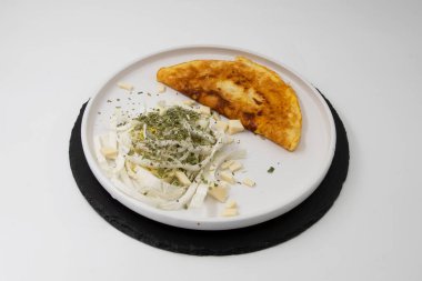 Kızarmış omlet, dilimlenmiş lahana peyniri ve beyaz tabakta kurutulmuş otlar.