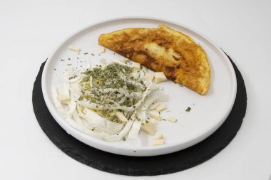 Kızarmış omlet, dilimlenmiş lahana peyniri ve beyaz tabakta kurutulmuş otlar.