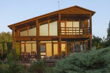 Kırsal kesimde gün batımında bahçeli ve balkonlu ahşap kır evi.