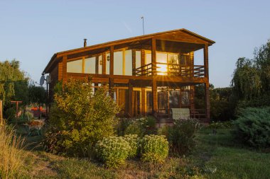 Kırsal kesimde gün batımında bahçeli ve balkonlu ahşap kır evi.