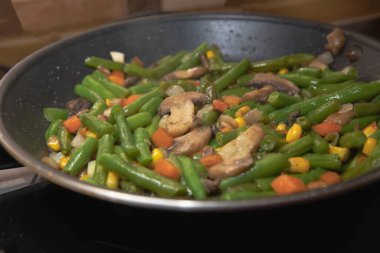 Donmuş sebzeler, yeşil fasulye mantarları, mısır ve tavada pişen havuçlar.