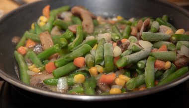 Donmuş sebzeler ve mantarlar indüksiyon sobasında tavada pişiyor.