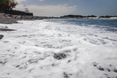 Deniz köpüğü ve plaj yüzeyine güneş ışığı yansıyan siyah volkanik kum.