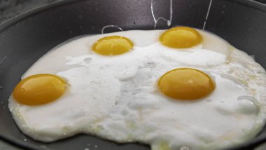 Dört yumurta, parlak yumurta sarısı, yapışmaz tavada pişiyor.