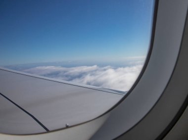 Bulutların üstünde açık mavi gökyüzünde görünen uçak kanadı.