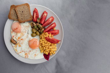 Kızarmış yumurta, mısır domatesli zeytin ve beyaz tabakta servis edilen ekmek.