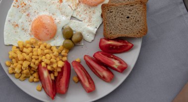 Kızarmış yumurta, mısır domatesli zeytin ve beyaz tabakta servis edilen ekmek.