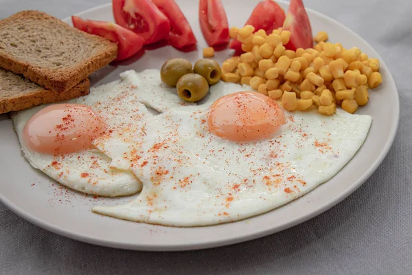 Kızarmış yumurta, mısır domatesli zeytin ve beyaz tabakta servis edilen ekmek.