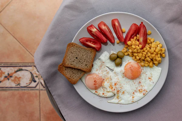 Kızarmış yumurta, mısır domatesli zeytin ve beyaz tabakta servis edilen ekmek.