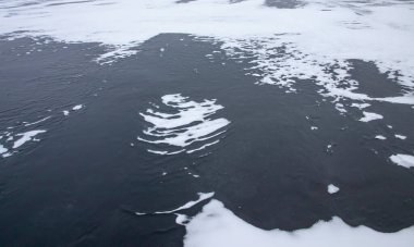 Donmuş su yüzeyinde karla çevrili ince buzlar açılıyor.