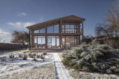 Güneşli bir günde, geniş pencereli ve kış bahçeli modern ahşap bir ev.