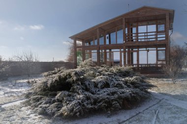 Güneşli bir günde, geniş pencereli ve kış bahçeli modern ahşap bir ev.