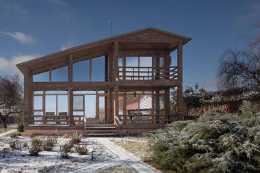 Güneşli bir günde, geniş pencereli ve kış bahçeli modern ahşap bir ev.