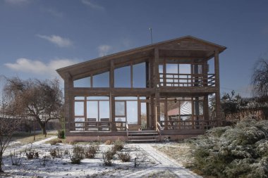 Güneşli bir günde, geniş pencereli ve kış bahçeli modern ahşap bir ev.