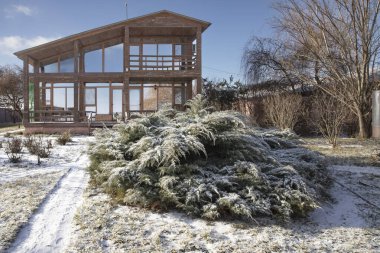 Güneşli bir günde, geniş pencereli ve kış bahçeli modern ahşap bir ev.