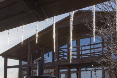 Kışın modern ahşap evin çatısından sarkan buz saçakları