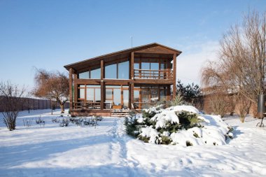 Karlı kış bahçesinde geniş pencereli modern ahşap ev