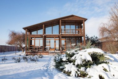 Karlı kış bahçesinde geniş pencereli modern ahşap ev