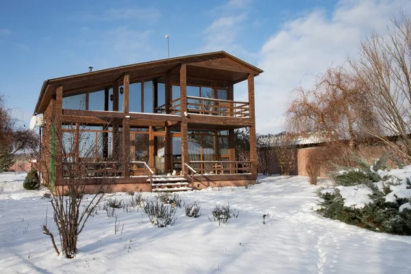 Kışın panoramik pencereleri ve karla kaplı özel bahçesi olan modern iki katlı ahşap kır evi.