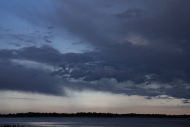 Sakin göl üzerinde kara fırtına bulutları alacakaranlıkta dramatik akşam gökyüzü ile su