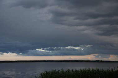 Sakin göl üzerinde kara fırtına bulutları alacakaranlıkta dramatik akşam gökyüzü ile su
