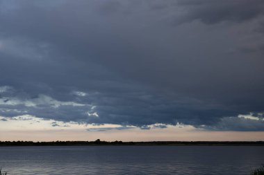 Sakin göl üzerinde kara fırtına bulutları alacakaranlıkta dramatik akşam gökyüzü ile su