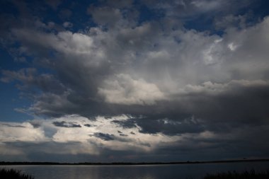 Sakin göl üzerindeki dramatik fırtına bulutları. Karanlık gökyüzü ve değişen hava atmosferi.