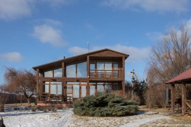 Kışın panoramik pencereleri ve terası olan modern ahşap kır evi.